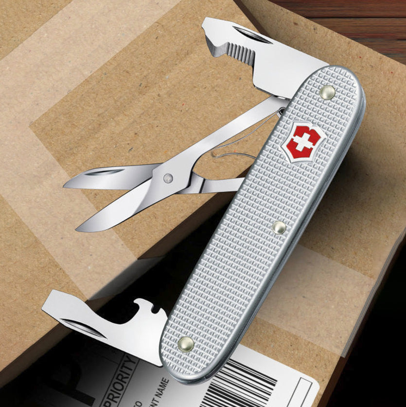 Multitool with knife, scissors, and bottle opener on a cardboard surface
