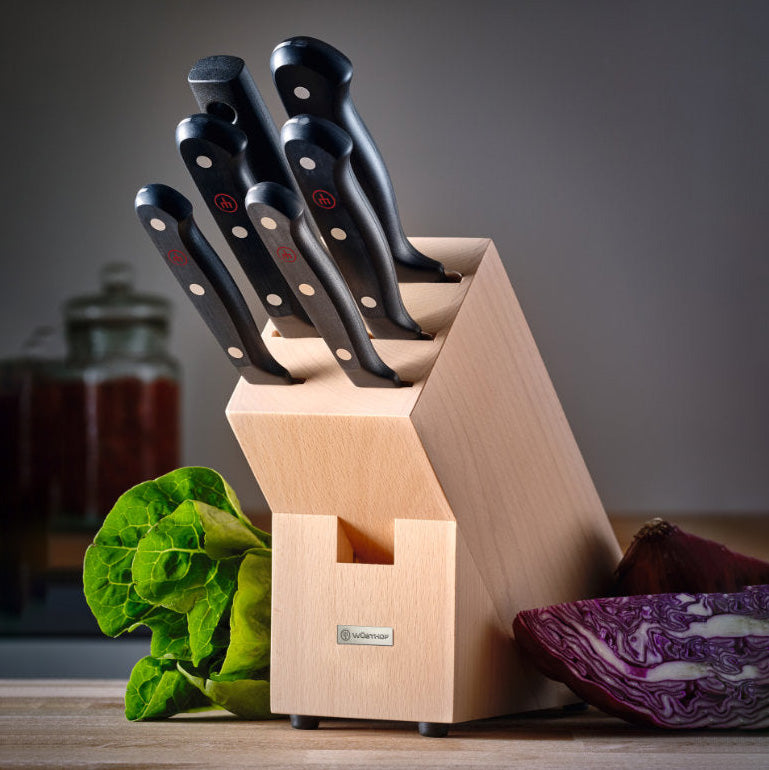 Set of knives in a wooden block with vegetables on a wooden surface