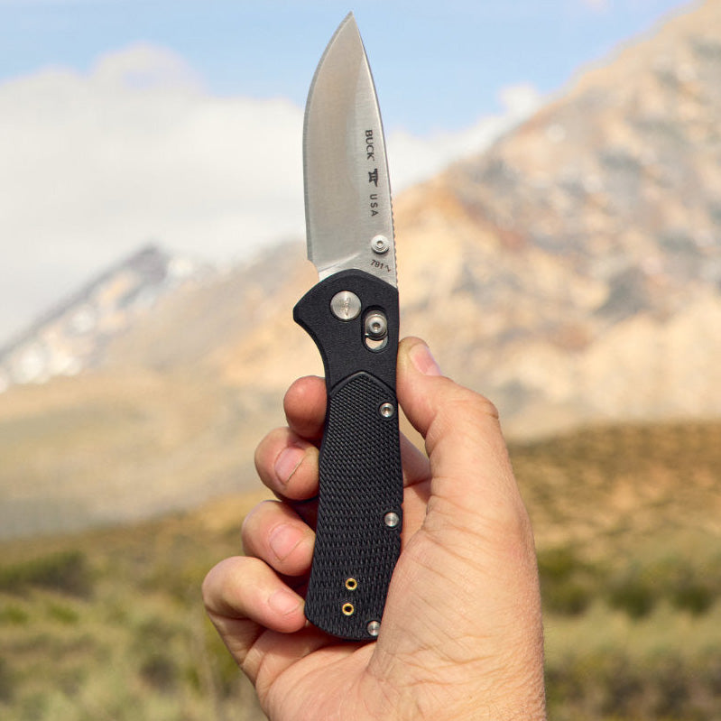 Folding knife held in a hand with mountains in the background